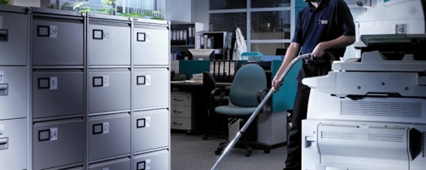 Agent d’entretien en uniforme sombre passant l’aspirateur dans un bureau